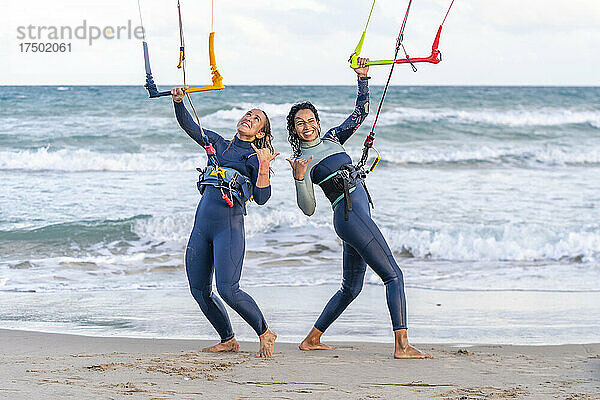 Fröhliche Freunde gestikulieren und Kitesurfen am Strand