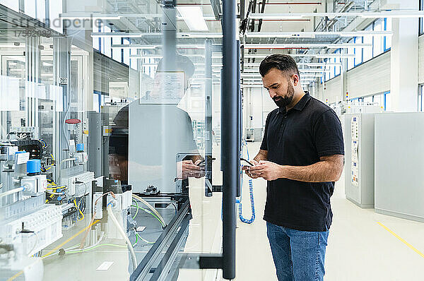Ingenieur benutzt Mobiltelefon an Industriemaschine hinter Glas