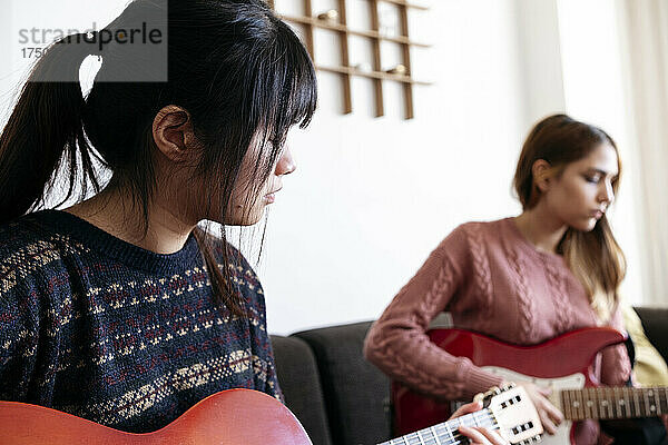 Junge Freunde spielen zu Hause gemeinsam Gitarre