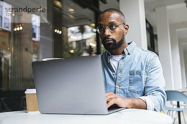 Nachdenklicher Mann mit Laptop sitzt im Straßencafé