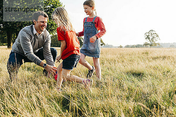 Fröhlicher Vater spielt mit Töchtern im öffentlichen Park