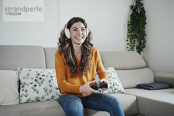 Glückliche Frau mit Kopfhörern  die zu Hause ein Spiel über den Joystick spielt