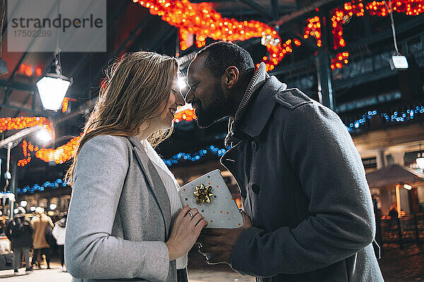 Mann mit Geschenkbox reibt Frau auf Weihnachtsmarkt die Nase