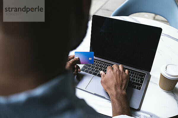 Mann tätigt Online-Zahlung am Laptop per Kreditkarte im Straßencafé
