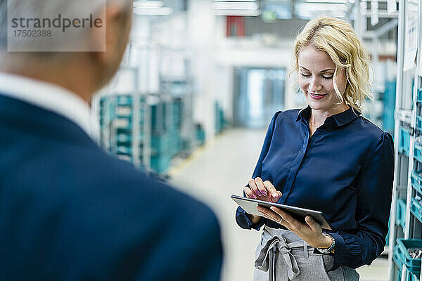 Lächelnde Geschäftsfrau nutzt Tablet-PC mit Kollegen in der Fabrik