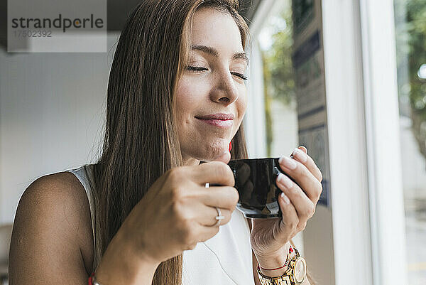 Frau mit geschlossenen Augen riecht Kaffee aus Tasse im Café