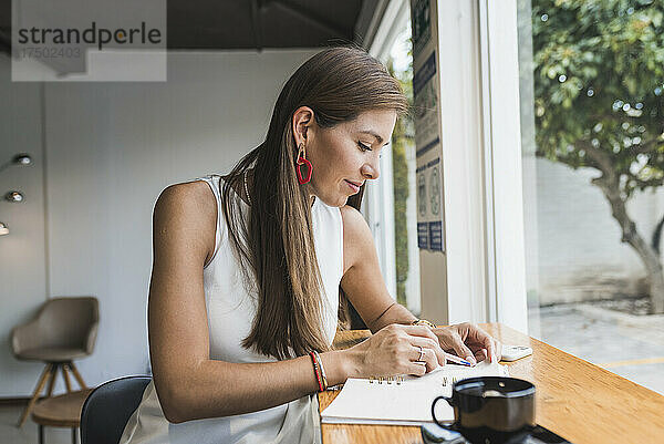 Frau schreibt Tagebuch und sitzt im Café