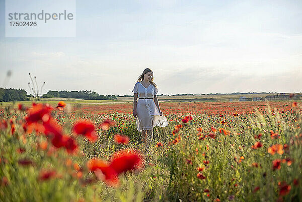 Junge Frau spaziert inmitten von Mohnblumen auf dem Feld