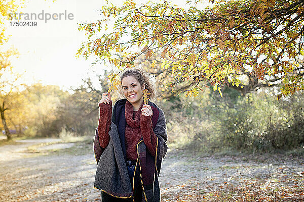 Lächelnde schöne Frau hält am Wochenende Herbstblätter im Wald