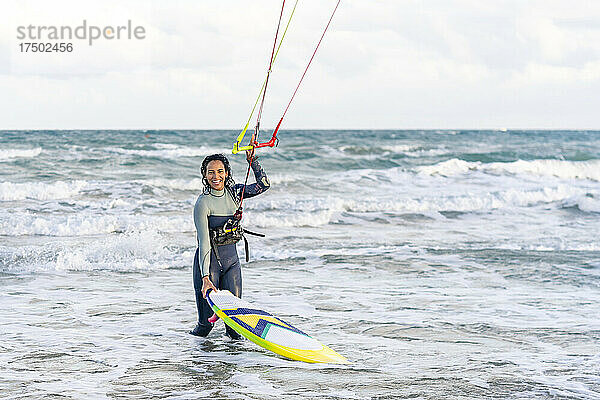 Lächelnde Frau hält im Urlaub den Griff eines Drachenfallschirms und eines Kiteboards im Wasser