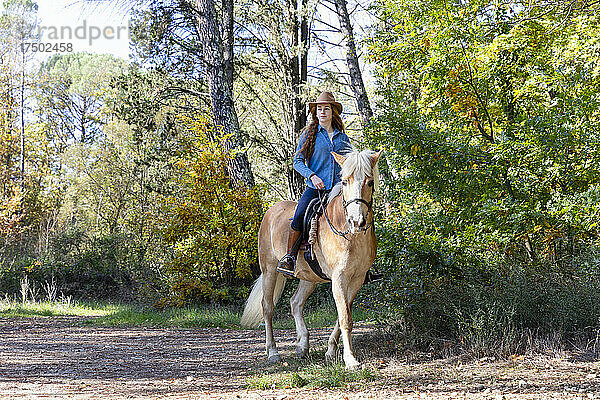 Frau mit Hut beim Reiten auf der Wiese