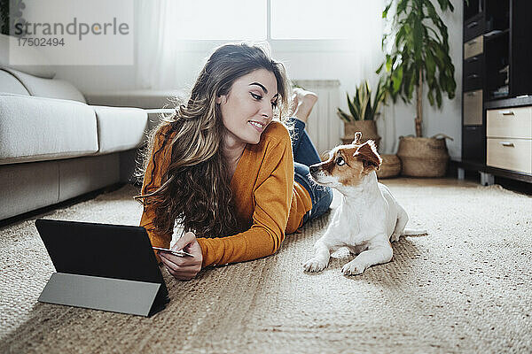 Junge Frau mit Tablet-PC schaut auf den am Boden liegenden Hund