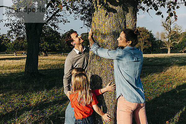Eltern und Töchter umarmen am Wochenende einen Baum im Park