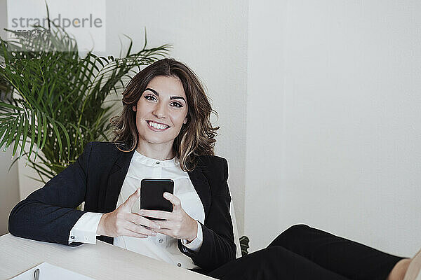 Berufstätige Frau mit Smartphone lächelt im Büro