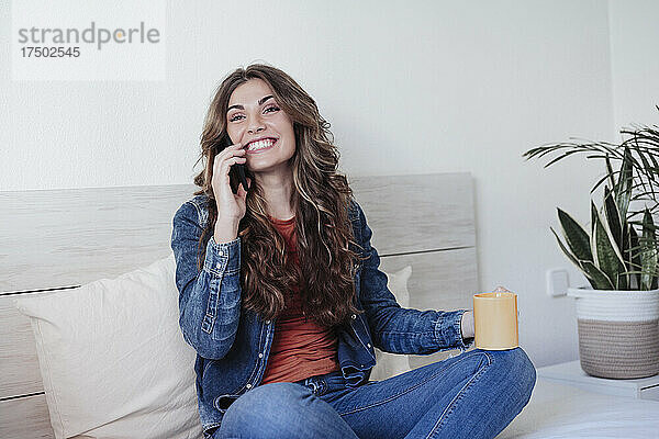 Glückliche Frau mit langen Haaren  die im Schlafzimmer mit dem Handy telefoniert