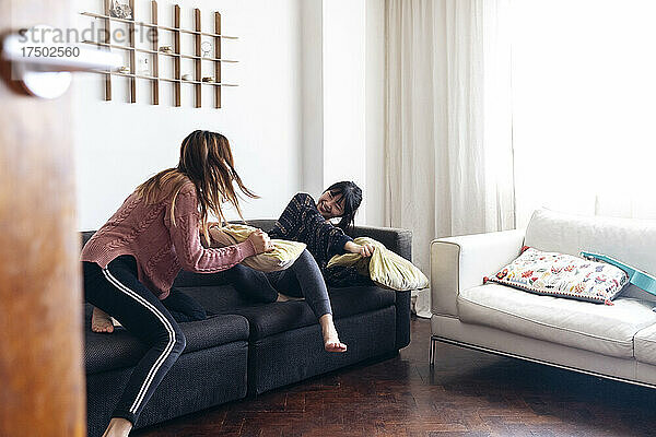 Fröhliche junge Freunde spielen mit Kissen auf dem Sofa im Wohnzimmer