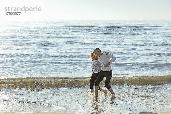 Verspieltes Paar genießt das Wasser am Strand