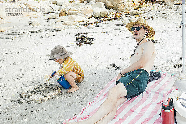 Lächelnder Mann und Sohn spielen im Sand am Strand