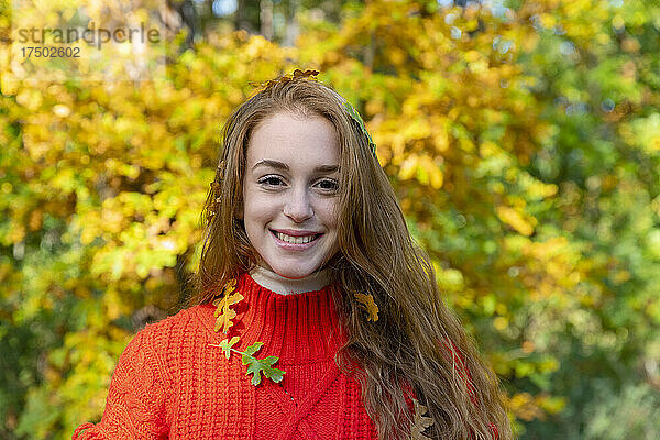 Lächelnde junge Frau mit Herbstblättern im Wald