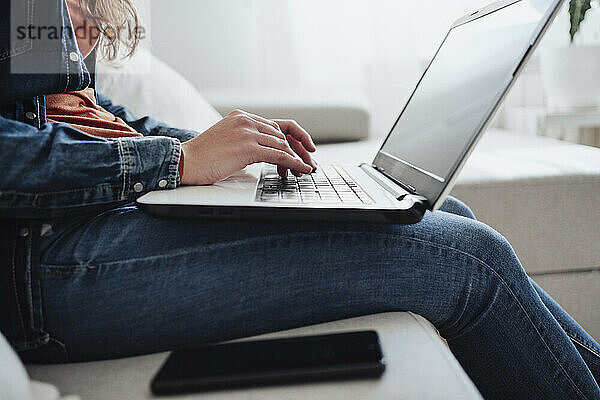 Junge Frau benutzt Laptop auf Sofa zu Hause