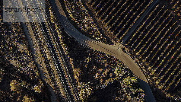 Luftaufnahme einer Landstraße  die sich in der Herbstdämmerung entlang der Bahngleise erstreckt