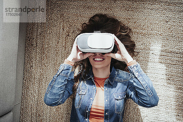 Lächelnde Frau mit Virtual-Reality-Headset liegt auf Teppich