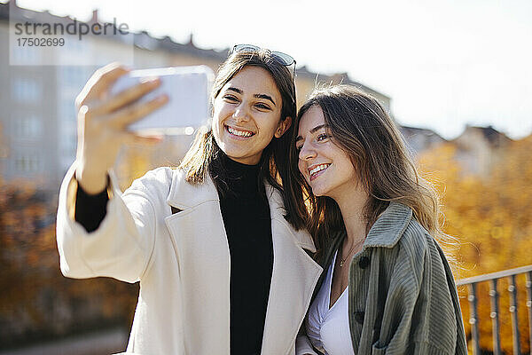 Lächelndes Teenager-Mädchen im Mantel macht ein Selfie mit einer Freundin im Park