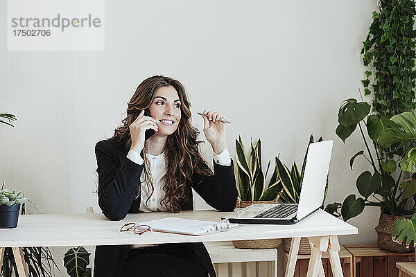 Lächelnde Geschäftsfrau  die im Büro mit dem Smartphone spricht