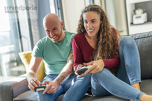 Lächelndes Paar mit Videospiel-Controller spielt auf dem Sofa