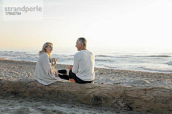 Ein Paar redet miteinander und sitzt auf einem Baumstamm am Strand