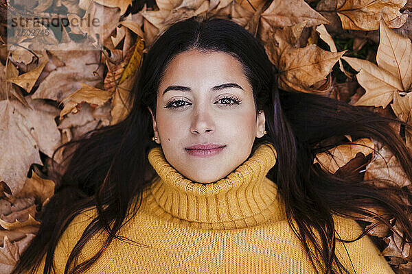 Junge Frau im Pullover liegt auf trockenem Herbstblatt