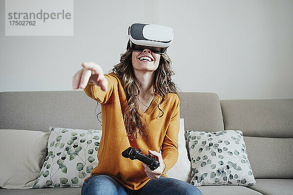 Frau gestikuliert mit Joystick und trägt zu Hause ein Virtual-Reality-Headset