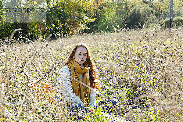 Junge Frau sitzt an einem sonnigen Tag im Gras