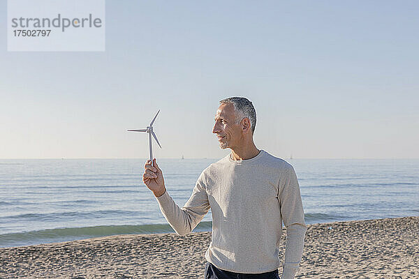 Mann blickt auf Windturbinenmodell  das am Strand steht