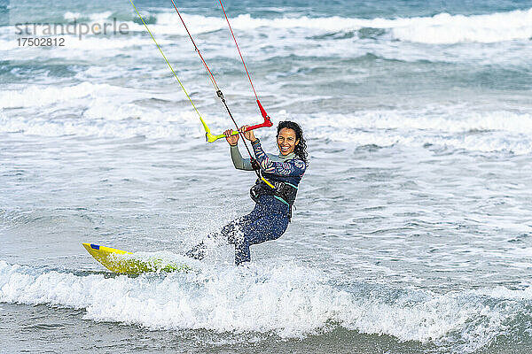 Fröhliche Frau surft mit Kiteboard auf dem Wasser