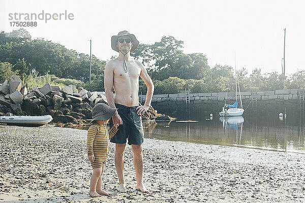 Hemdloser Mann steht mit Sohn im Urlaub im Sand am Strand