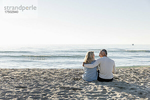 Mann mit Arm um Frau  die zusammen im Sand am Strand sitzt