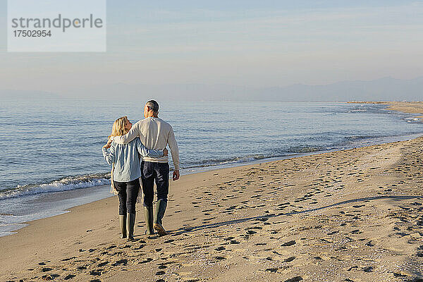 Paar mit Arm umeinander beim Spaziergang am Strand