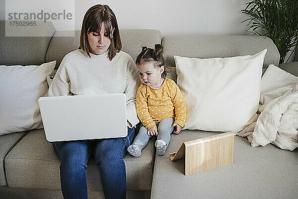Mutter nutzt Laptop  Tochter mit Tablet-PC auf Sofa
