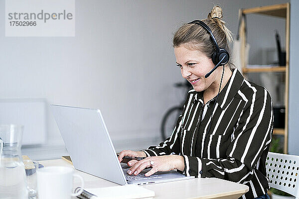 Geschäftsfrau mit Kopfhörern nutzt Laptop im Heimbüro