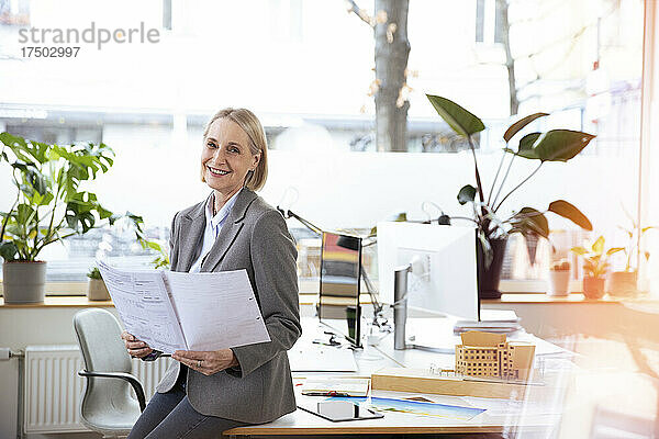 Lächelnde Geschäftsfrau hält Dokumente im Büro