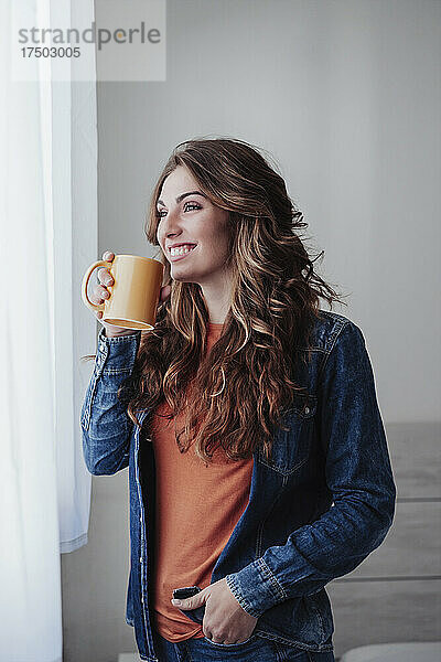 Glückliche junge Frau  die am Fenster Kaffee trinkt