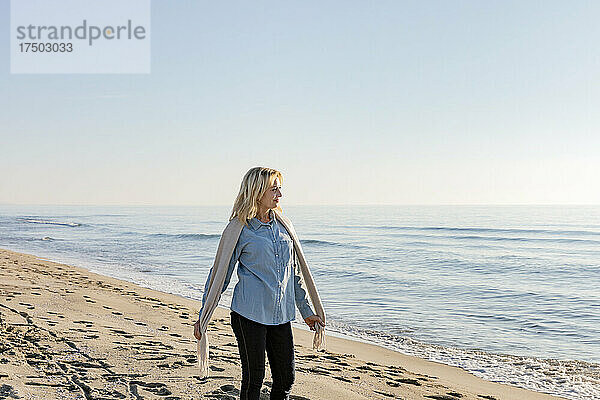 Frau mit Schal steht am Strand