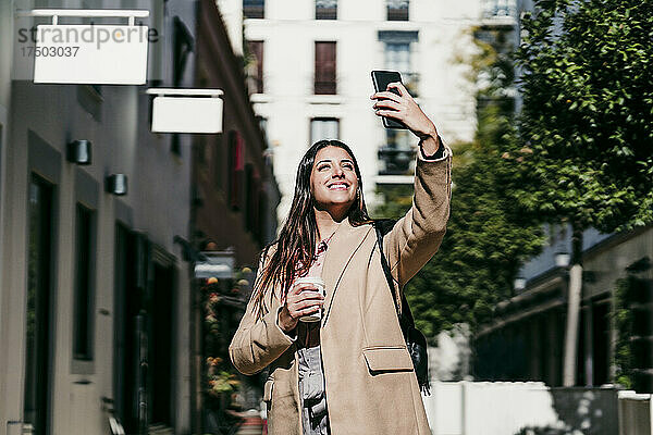 Lächelnde Geschäftsfrau  die an einem sonnigen Tag ein Selfie mit dem Smartphone macht