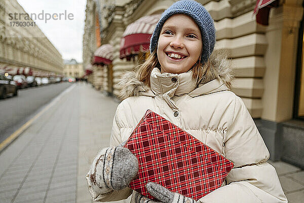 Glückliches Mädchen hält verpacktes Weihnachtsgeschenk in der Stadt