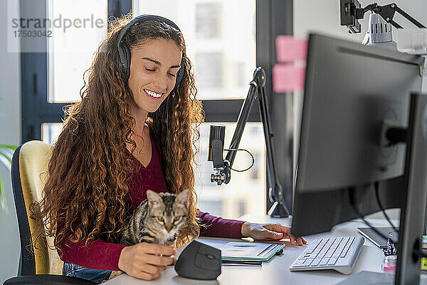 Lächelnde junge Frau blickt auf die Katze auf dem Schreibtisch