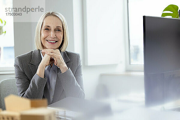 Lächelnde Geschäftsfrau mit den Händen am Kinn im Büro