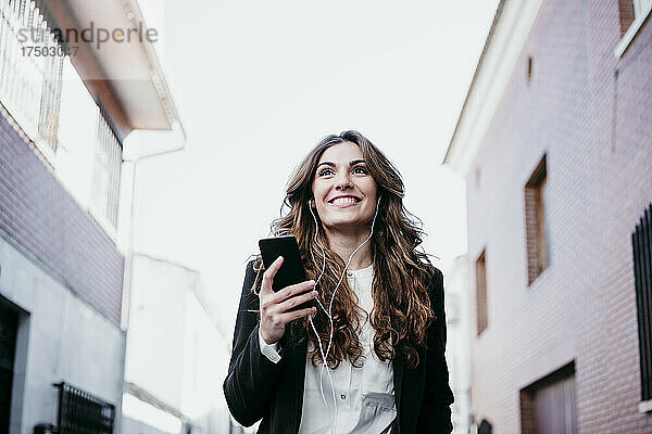 Lächelnde Geschäftsfrau  die Musik auf dem Smartphone hört