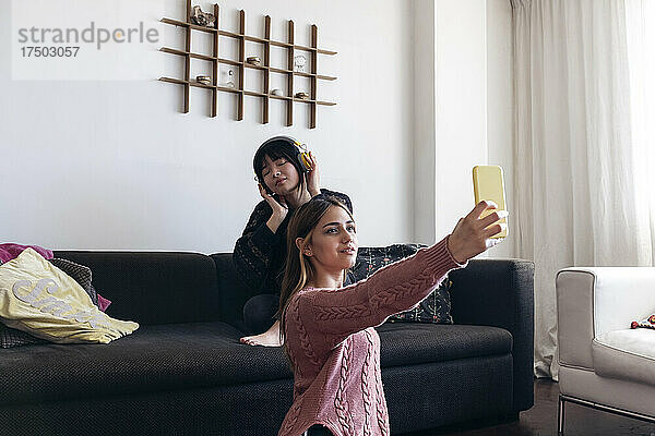 Frau macht Selfie per Smartphone mit Freund  der auf dem Sofa Musik hört