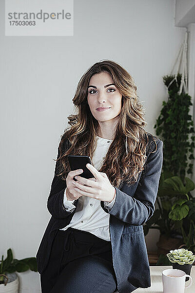 Geschäftsfrau mit braunen Haaren hält Smartphone im Büro